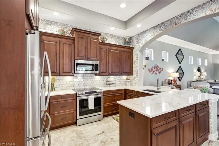 Kitchen with appliances with stainless steel finishes, backsplash, light stone counters, a peninsula, and brown cabinetry