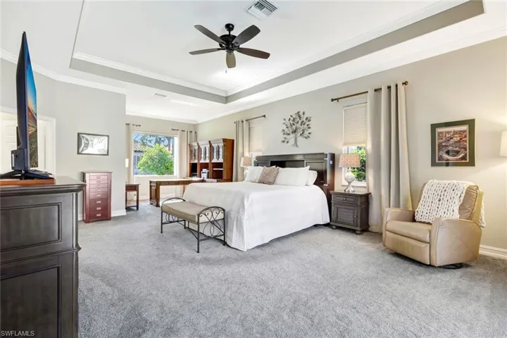 Bedroom featuring a tray ceiling, light carpet, ceiling fan, and ornamental molding