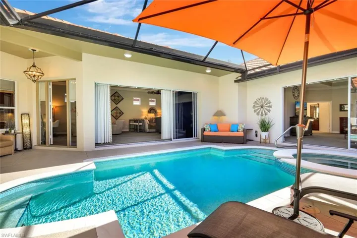 Outdoor pool featuring glass enclosure, a patio area, a sunroom, and an in-ground hot tub