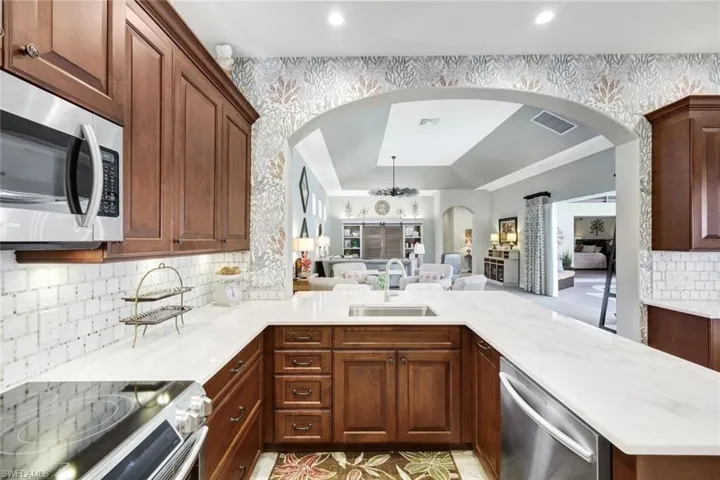 Kitchen with appliances with stainless steel finishes, backsplash, open floor plan, arched walkways, and light stone counters