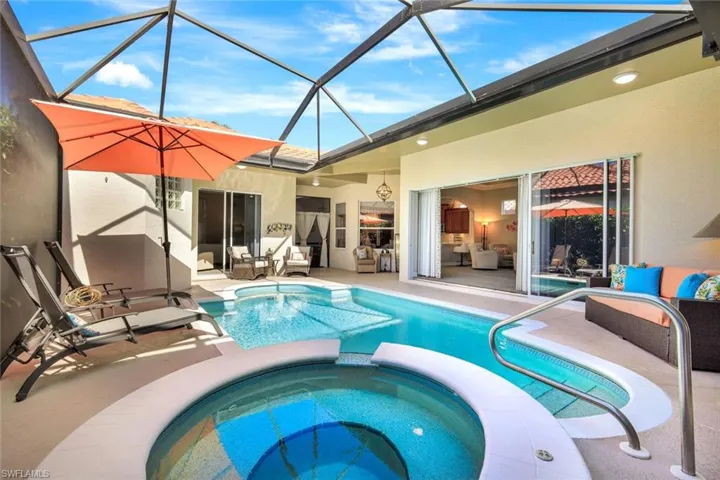 View of swimming pool featuring glass enclosure, a sunroom, a pool with connected hot tub, and a patio area
