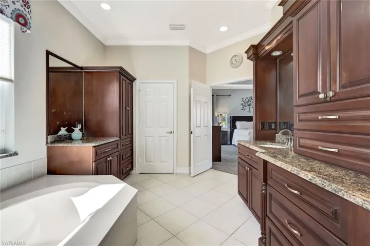 Ensuite bathroom with vanity, ornamental molding, a garden tub, and light tile patterned floors