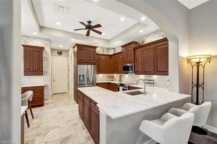 Kitchen with arched walkways, light stone countertops, stainless steel appliances, a peninsula, and a kitchen bar