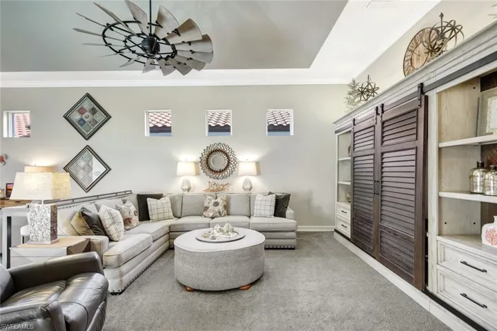 Living area with a barn door, light colored carpet, crown molding, and ceiling fan
