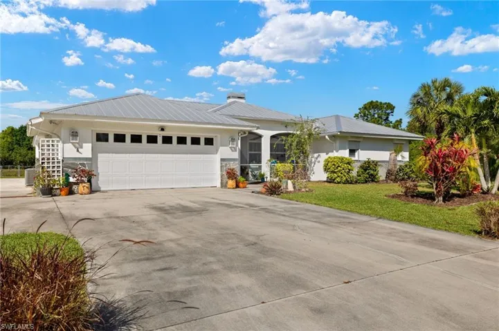 Ranch-style home featuring metal roof, a garage, concrete driveway, stucco siding, and a front yard