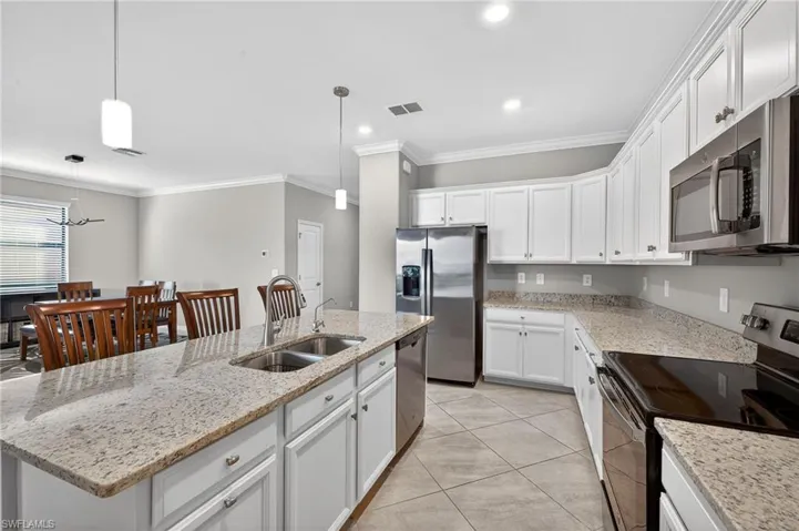 Kitchen featuring stainless steel appliances, a kitchen island with sink, light stone countertops, white cabinets, and ornamental molding