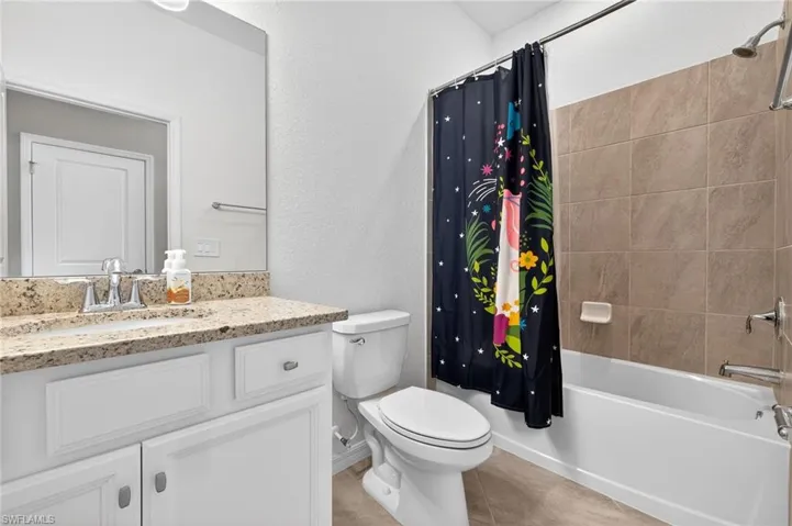 Full bathroom featuring a textured wall, vanity, shower / bathtub combination with curtain, and light tile patterned floors