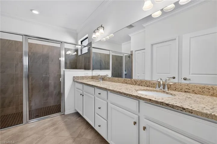 Bathroom featuring double vanity, a stall shower, crown molding, and light tile patterned floors