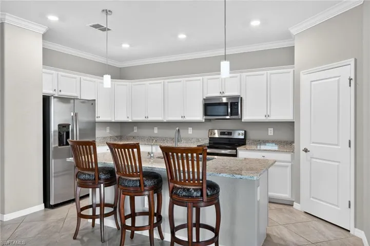Kitchen with white cabinetry, stainless steel appliances, a kitchen breakfast bar, ornamental molding, and an island with sink