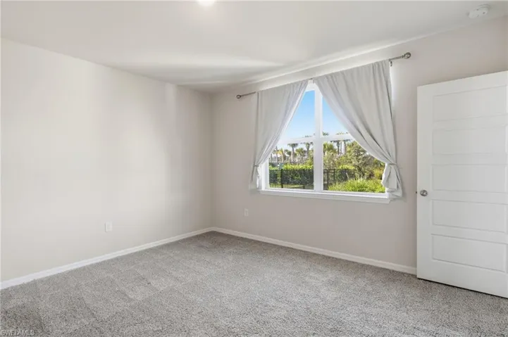 Bright interior room featuring a large window with exterior greenery, neutral wall color, and plush gray carpeting