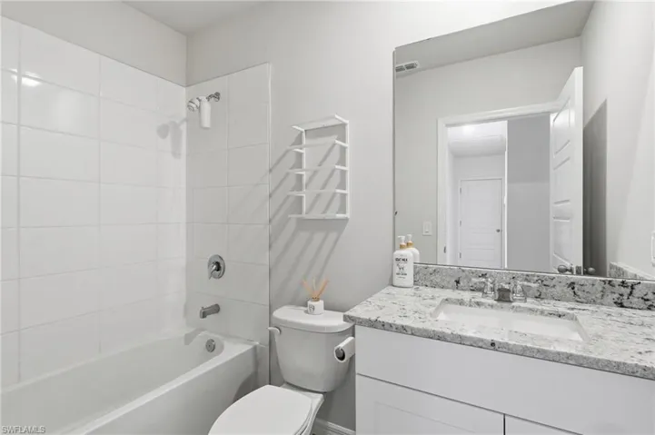 Bathroom featuring a white bathtub with subway tile surround, polished chrome fixtures, and a vanity with a light-colored stone countertop