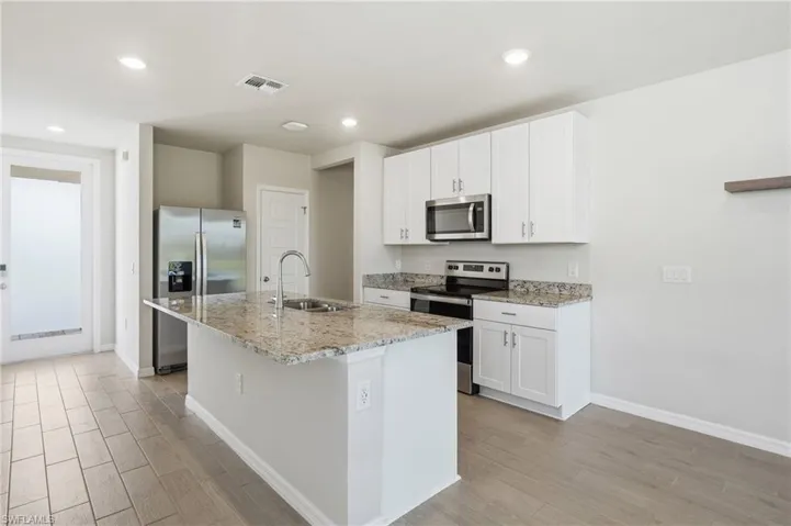Modern kitchen featuring an island with a stainless steel sink, granite countertops, white cabinetry, stainless steel appliances, and wood-finish flooring
