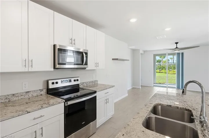 Modern kitchen featuring white cabinetry, stainless steel appliances, speckled countertops, and a double basin sink with a high-arch faucet