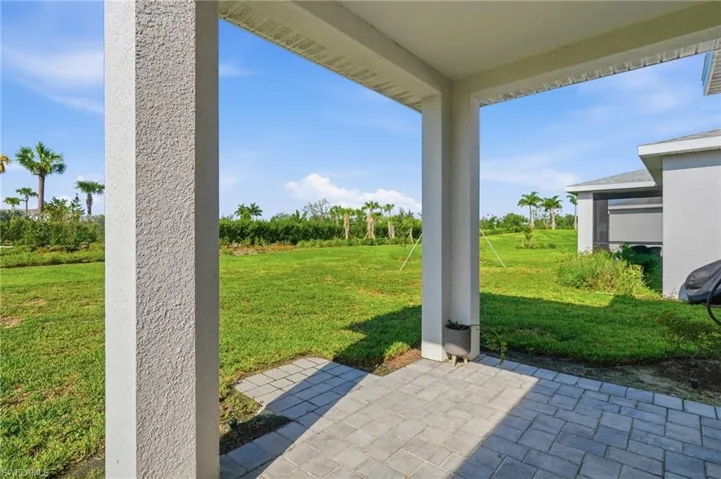 Covered patio with paver flooring, stucco columns, and expansive green space