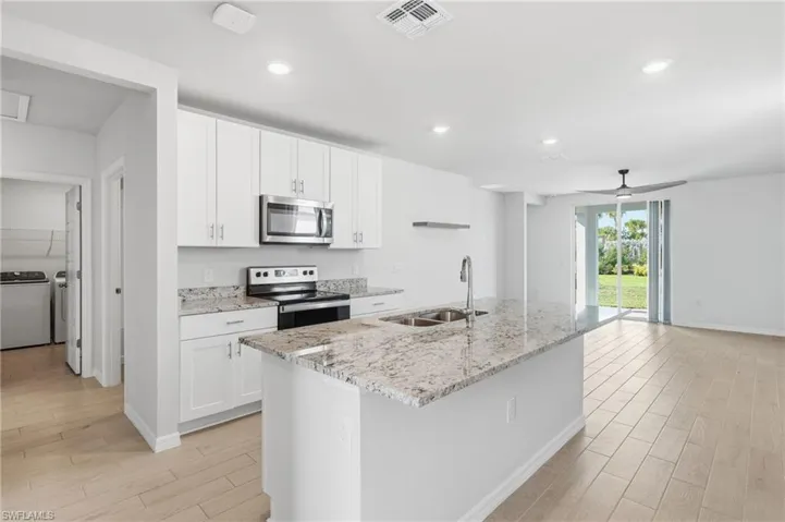 Kitchen featuring white cabinetry, stainless steel appliances, granite countertops, an island with an undermount double sink, and wood-finish flooring