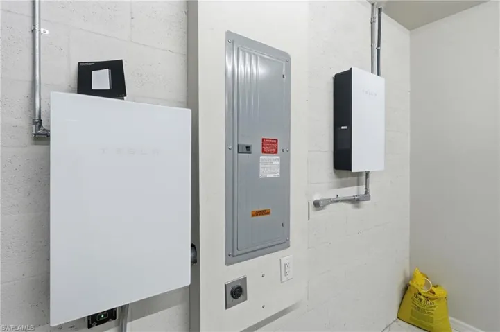 Integrated white-panel energy storage systems with conduit wiring, alongside an electrical service panel and wall outlets