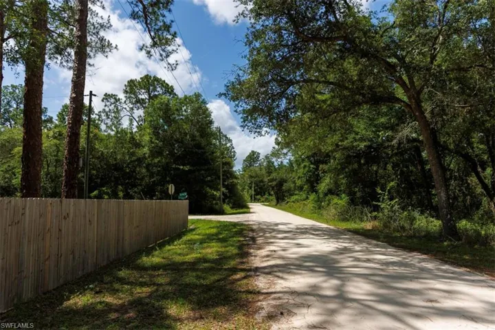 Fenced property border along a gravel road, surrounded by mature trees and natural landscaping