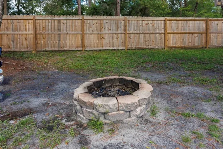 Backyard featuring a stone-stacked fire pit, a wooden privacy fence, and a combination of grass and natural ground cover