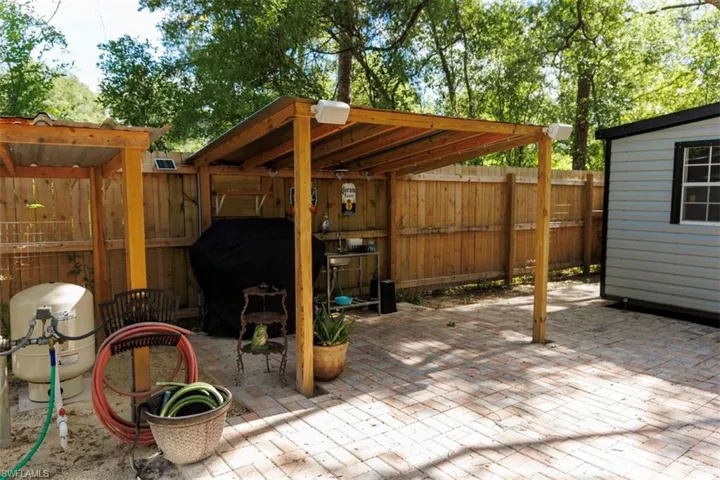 Expansive paver patio with a wood-framed covered outdoor kitchen area, featuring a built-in sink and wood privacy fencing