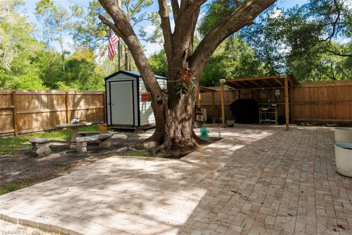 Expansive backyard featuring a paver patio, a large mature tree, a covered outdoor structure, a storage shed, and a privacy fence