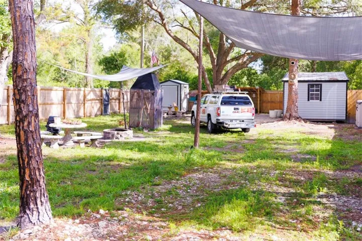 Expansive yard featuring a privacy fence, two storage sheds, and mature trees