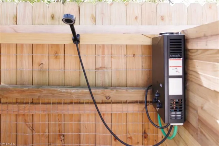 Outdoor shower system featuring a portable water heater and a handheld shower head, installed against a wood privacy fence