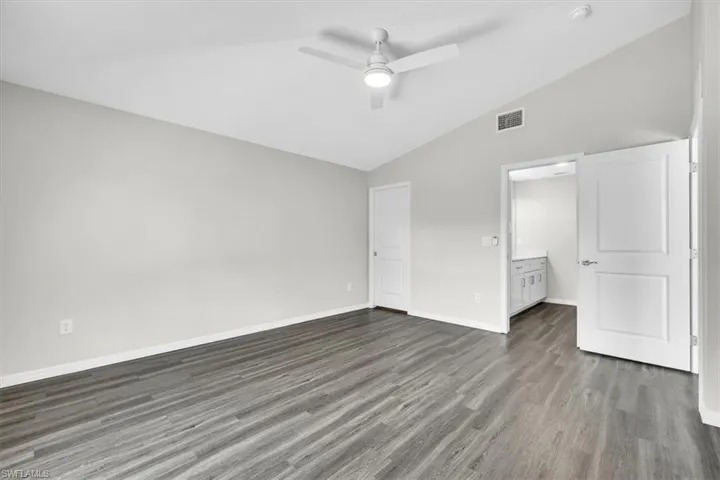 Unfurnished bedroom with lofted ceiling, dark wood-style floors, ceiling fan, and connected bathroom