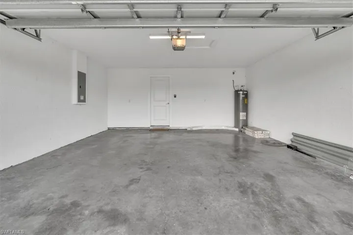 Garage with electric panel, electric water heater, and a garage door opener