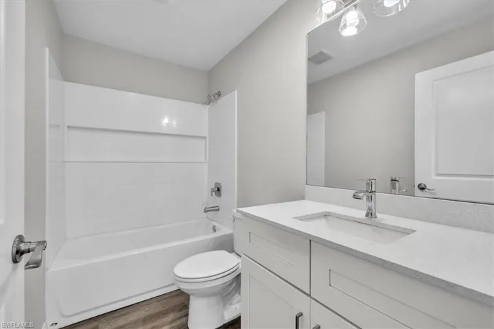 Bathroom with washtub / shower combination, vanity, and dark wood-type flooring