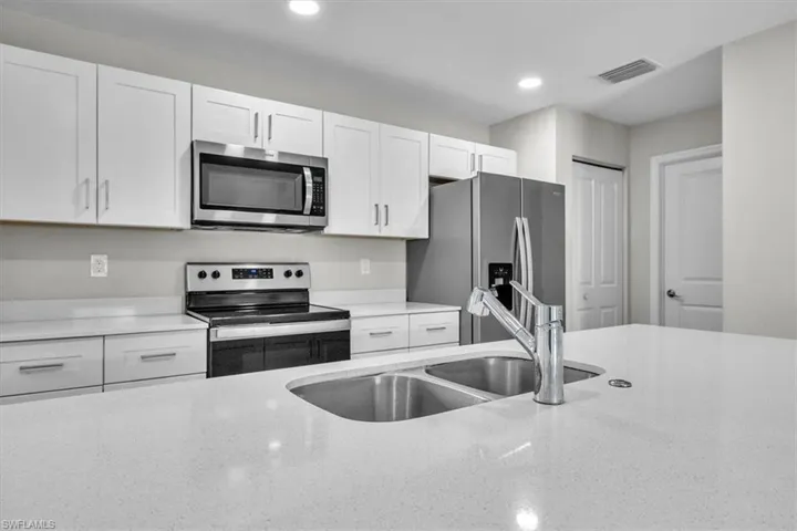Kitchen featuring appliances with stainless steel finishes, white cabinetry, recessed lighting, and light stone countertops