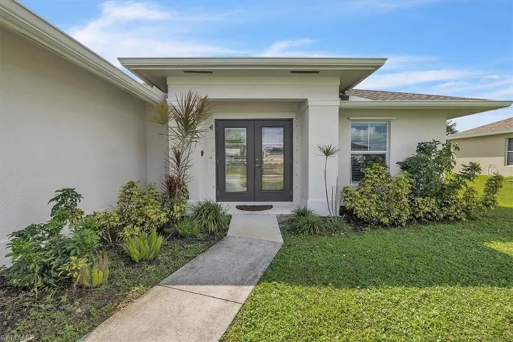 Property entrance featuring stucco siding, a lawn, and french doors