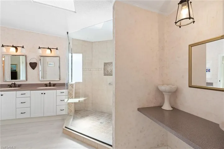 Bathroom featuring a tile shower, double vanity, a skylight, and a sink