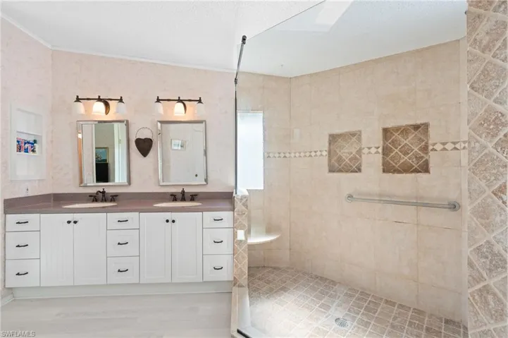 Full bath with double vanity, crown molding, a tile shower, and a sink