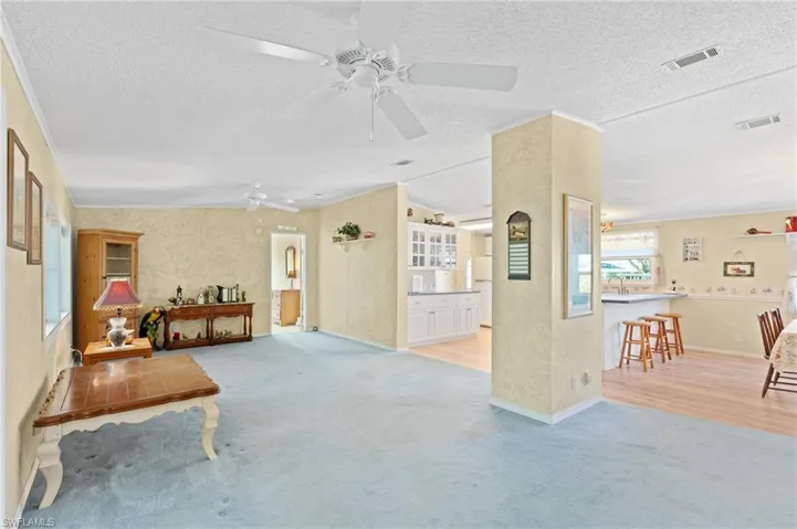 Carpeted living room with a sink, visible vents, a textured ceiling, and a ceiling fan