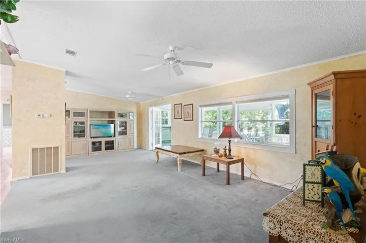 Carpeted living area with visible vents, lofted ceiling, a textured ceiling, and ceiling fan