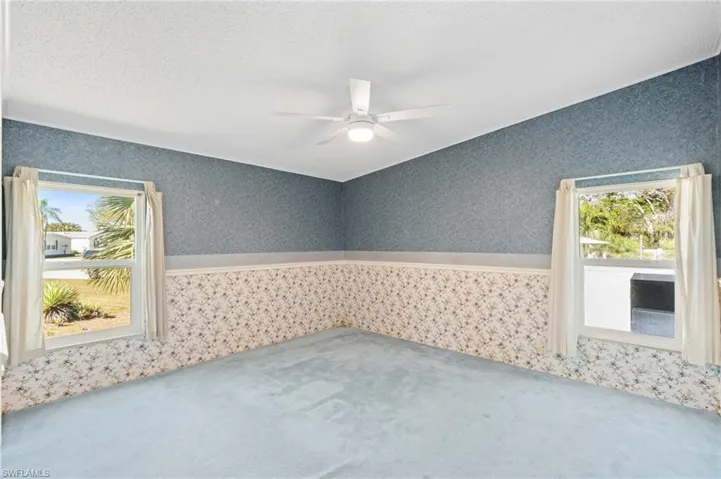 Spare room featuring wallpapered walls, carpet flooring, a wainscoted wall, and ceiling fan