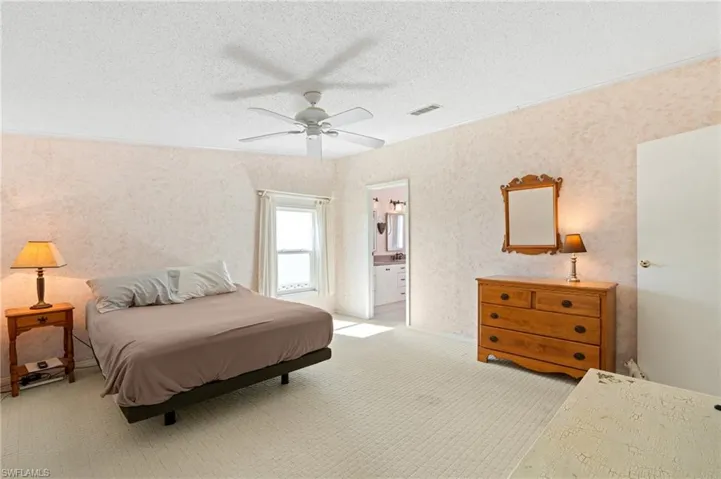 Bedroom with visible vents, a ceiling fan, a textured ceiling, connected bathroom, and light colored carpet