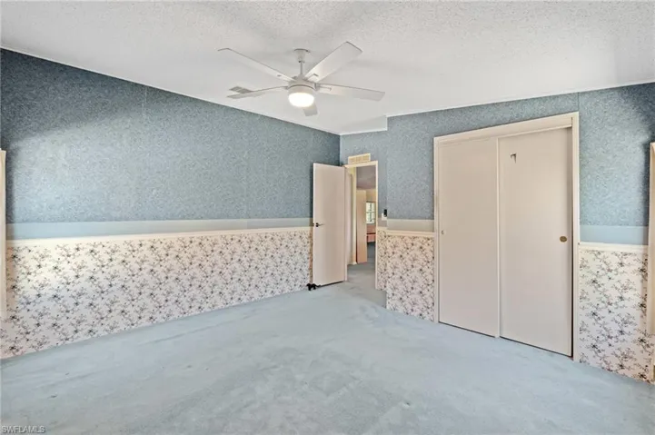 Unfurnished bedroom featuring a ceiling fan, wallpapered walls, a closet, a textured ceiling, and carpet flooring