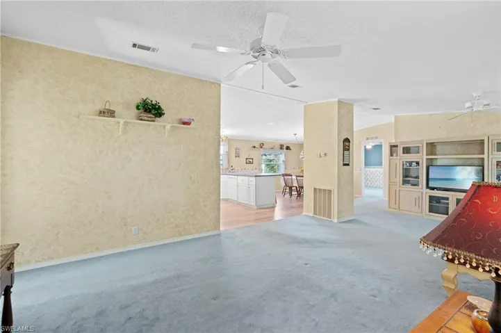 Unfurnished living room featuring visible vents, light carpet, a textured ceiling, and a ceiling fan