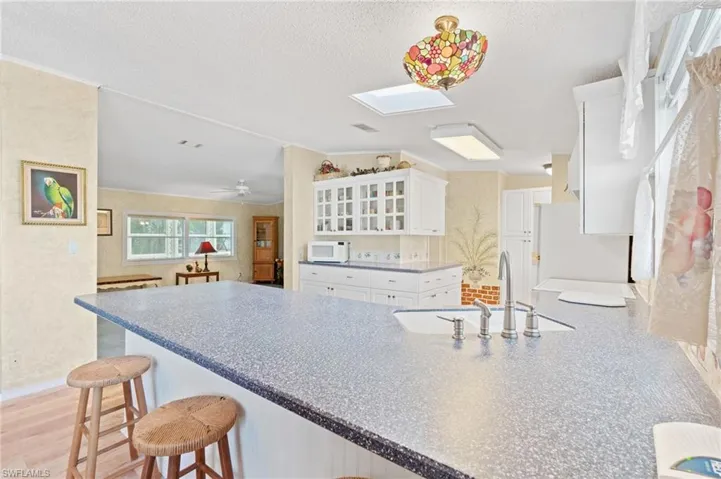 Kitchen with lofted ceiling with skylight, a sink, white appliances, white cabinets, and glass insert cabinets