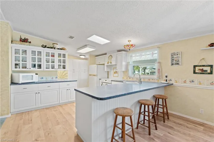Kitchen featuring light wood-style flooring, white appliances, a kitchen bar, and a peninsula