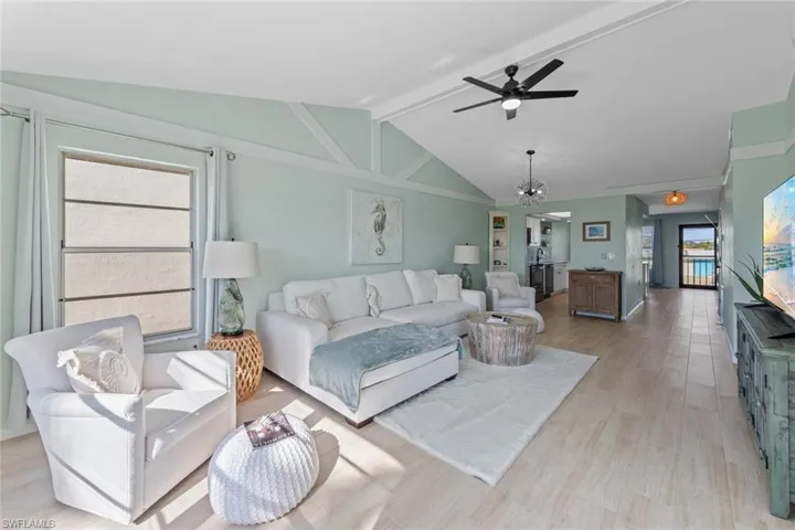 Living room featuring ceiling fan with notable chandelier, vaulted ceiling with beams, light hardwood / wood-style floors, and a wealth of natural light