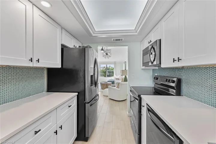 Kitchen with appliances with stainless steel finishes, backsplash, a raised ceiling, crown molding, and white cabinetry