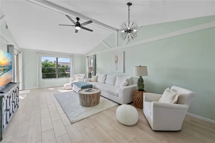 Living room with lofted ceiling with beams and ceiling fan with notable chandelier