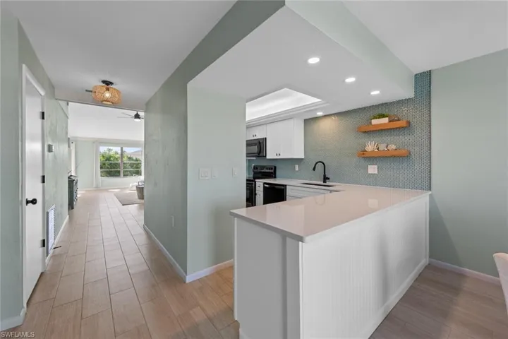 Kitchen with kitchen peninsula, ceiling fan, sink, black appliances, and white cabinets