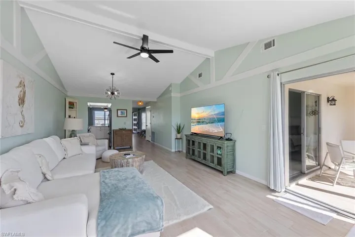 Living room featuring ceiling fan with notable chandelier, vaulted ceiling with beams, and light hardwood / wood-style flooring