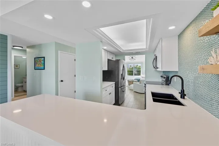 Kitchen featuring kitchen peninsula, appliances with stainless steel finishes, a raised ceiling, sink, and white cabinets