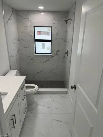 Bathroom featuring vanity, tile patterned flooring, a tile shower, and toilet