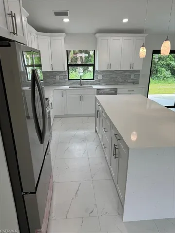 Kitchen featuring refrigerator, white cabinetry, decorative backsplash, and sink