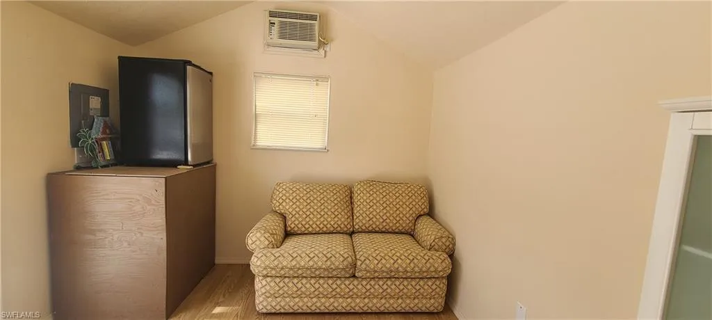 Living area with vaulted ceiling, wood finished floors, and an AC wall unit